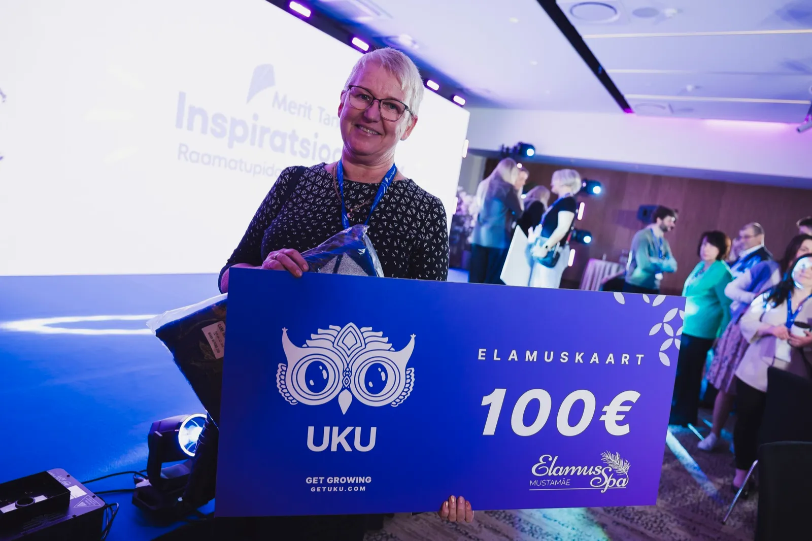Uku loosiauhinna võitja hoiab käes suurt Uku 100 euro elamuskaarti Elamus Spasse Meriti Inspiratsioonipäeval 2026