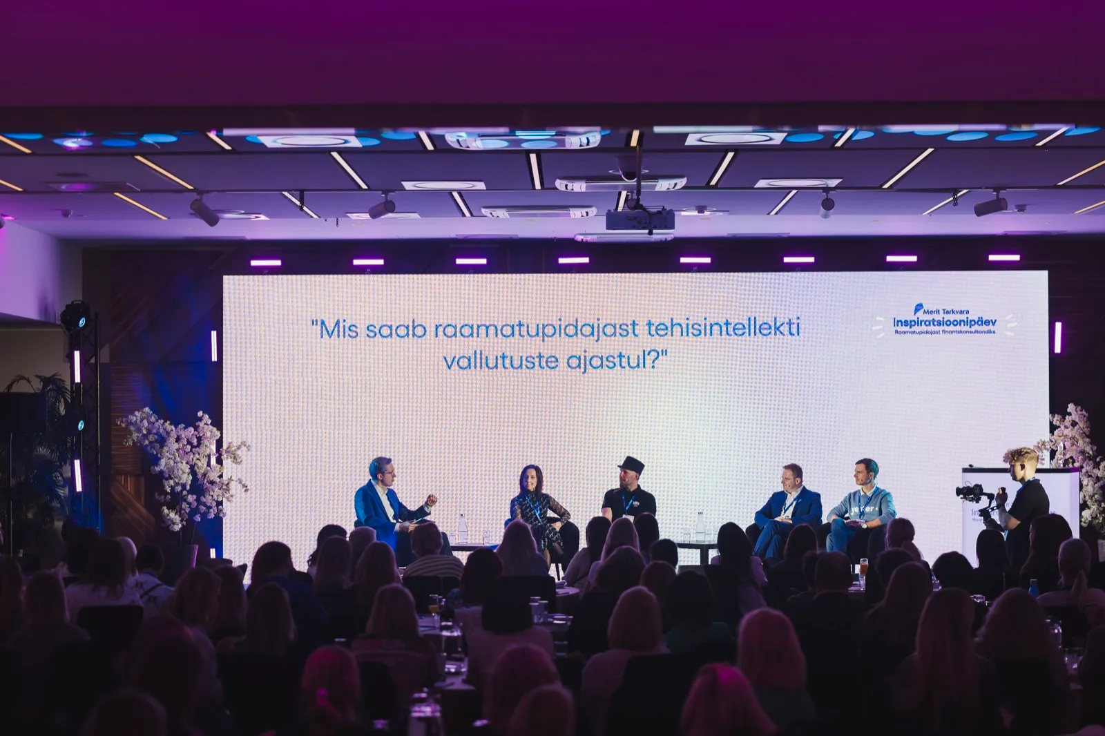 Paneelarutelu Meriti Inspiratsioonipäeval 2026: viis panelisti laval, nende taga ekraanil küsimus „Mis saab raamatupidajast tehisintellekti vallutuste ajastul?“, saalis täis publik