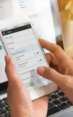 The CCH Axcess mobile app on a phone, partly covered by a hand — Home with Contacts, Notes, Responsible Staff and Accounts Receivable